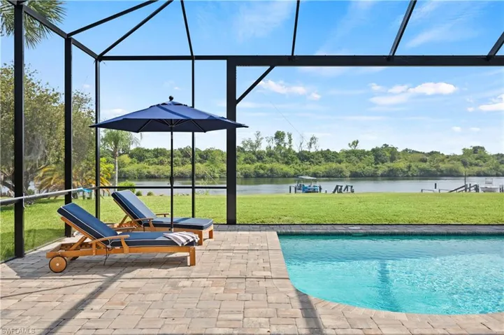 Screened-in pool area featuring a curved swimming pool, paver decking, and waterfront access with a boat dock