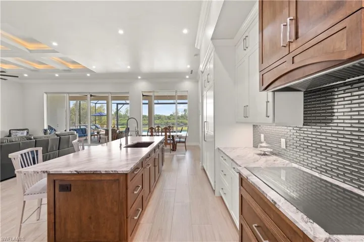 Expansive kitchen featuring a large island with an integrated sink, wood-finish cabinetry, light-toned countertops, and a tiled backsplash
