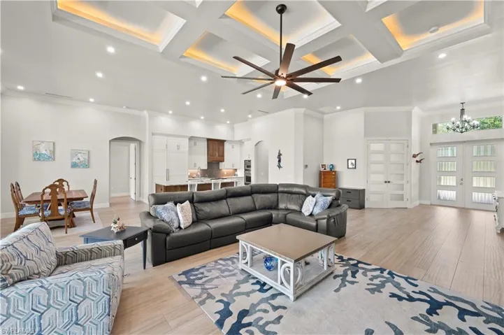 Spacious living area featuring coffered ceilings with accent lighting, a large ceiling fan, recessed lighting, and light wood-finish flooring