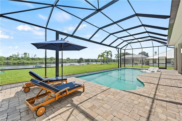 Screened outdoor living area featuring a swimming pool, paver patio, and direct waterfront access with expansive grassy areas