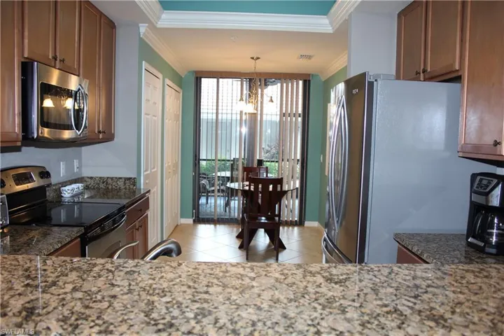 Kitchen with stainless steel appliances, crown molding, dark stone countertops, light tile patterned floors, and suspended lighting