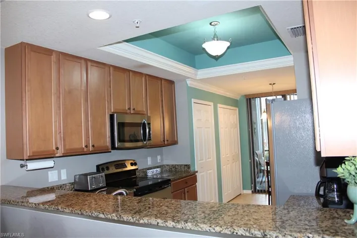 Kitchen with stainless steel appliances, wood finish cabinets, ornamental molding, a raised ceiling, and dark stone countertops