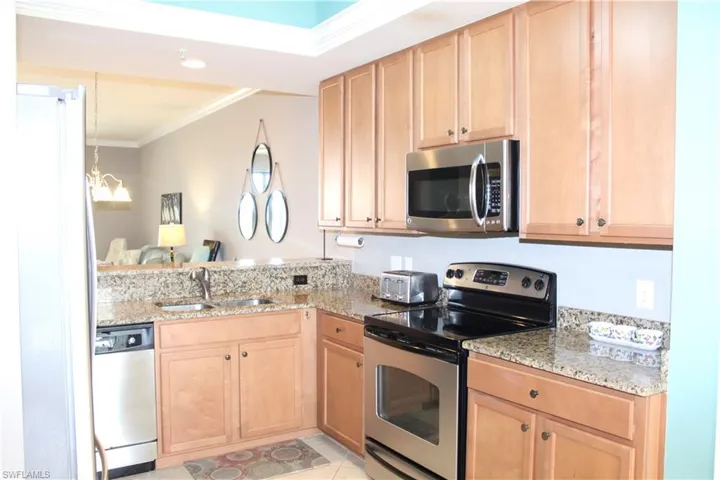 Kitchen featuring stainless steel appliances, light stone countertops, crown molding, light wood finish cabinets, and a peninsula