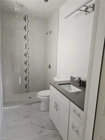 Bathroom featuring vanity, tile patterned flooring, a tile shower, and toilet