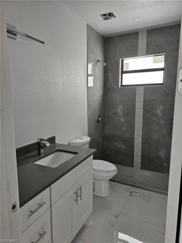 Bathroom featuring vanity, tiled shower, tile patterned flooring, and toilet