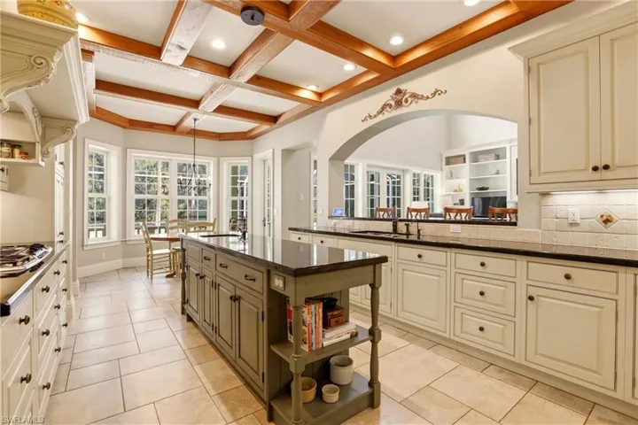 Kitchen featuring open shelves, decorative backsplash, coffered ceiling, dark stone counters, and light tile patterned floors