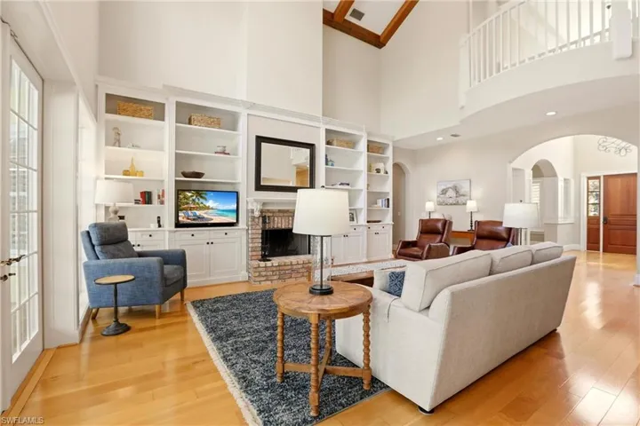 Living room with arched walkways, a fireplace, light wood-style flooring, and built in shelves