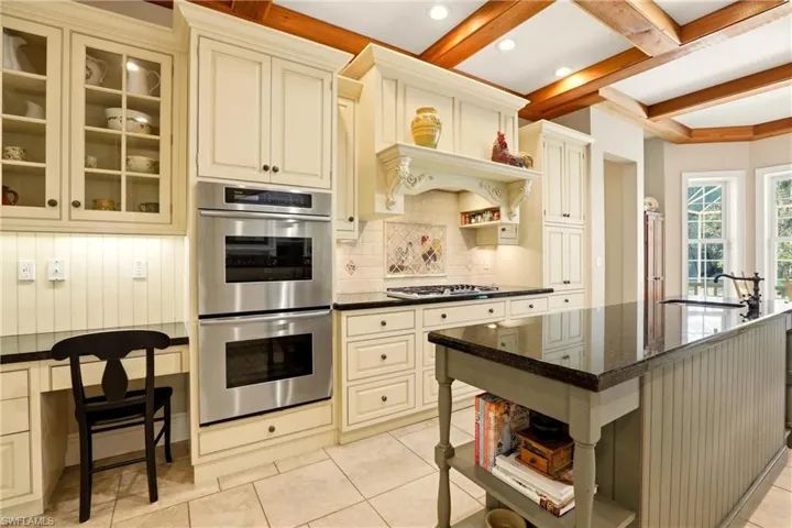 Kitchen with open shelves, stainless steel appliances, glass insert cabinets, cream cabinets, and an island with sink