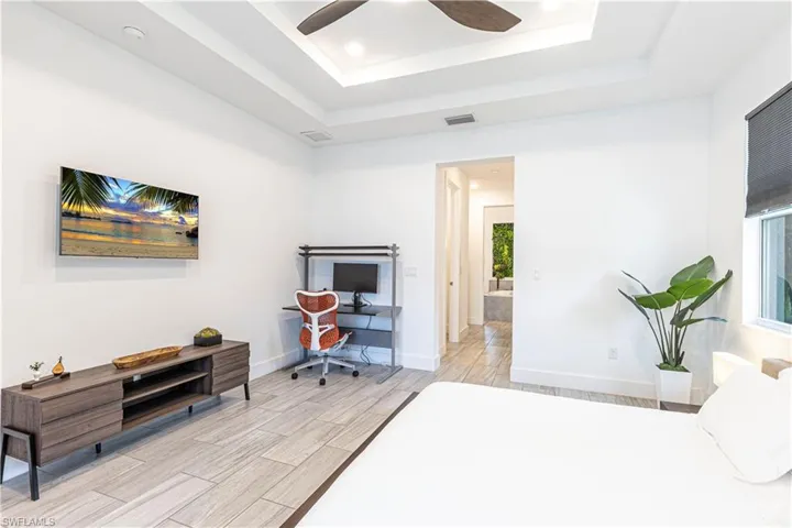 Bedroom with a tray ceiling, wood tiled floors, baseboards, a ceiling fan, and recessed lighting