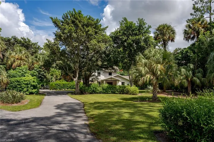Lush tropical landscaping surrounds this residence, featuring a private driveway, mature palm trees, diverse greenery, and a manicured lawn
