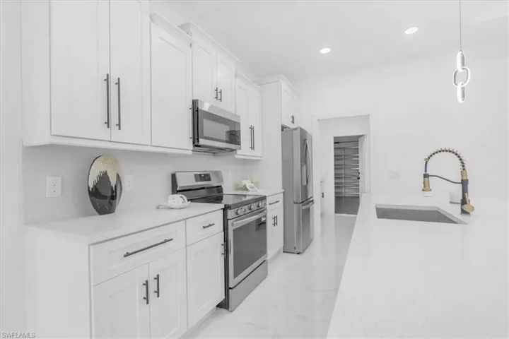 Kitchen featuring stainless steel appliances, light stone countertops, white cabinetry, pendant lighting, and light marble finish flooring