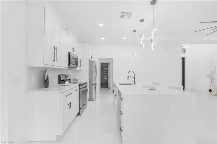Kitchen with stainless steel appliances, white cabinets, hanging light fixtures, light stone countertops, and recessed lighting