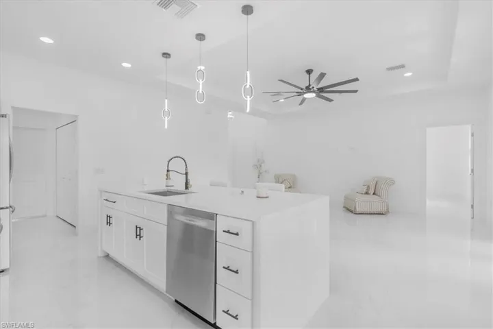 Kitchen featuring white cabinetry, light marble finish floors, dishwasher, pendant lighting, and light stone counters