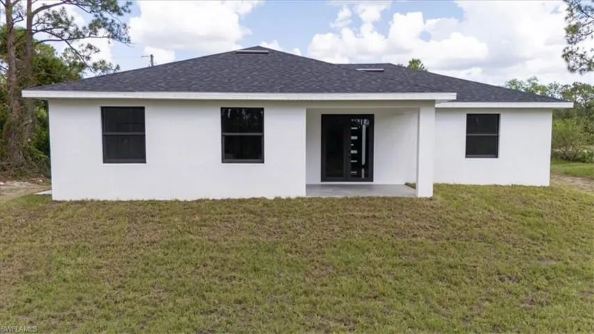 Rear view of property with a lawn, roof with shingles, and a patio