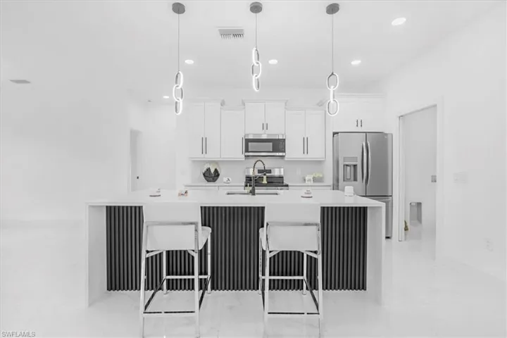 Kitchen with appliances with stainless steel finishes, light stone countertops, white cabinets, a kitchen breakfast bar, and a center island with sink