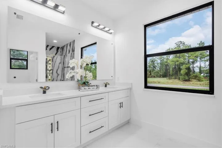 Full bath featuring a marble finish shower, light marble finish floors, and double vanity