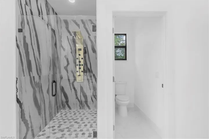 Bathroom with a marble finish shower and light marble finish flooring