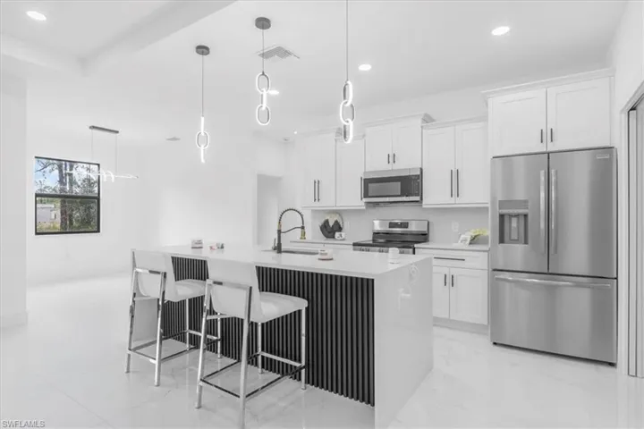 Kitchen with stainless steel appliances, pendant lighting, white cabinets, a breakfast bar area, and light stone counters