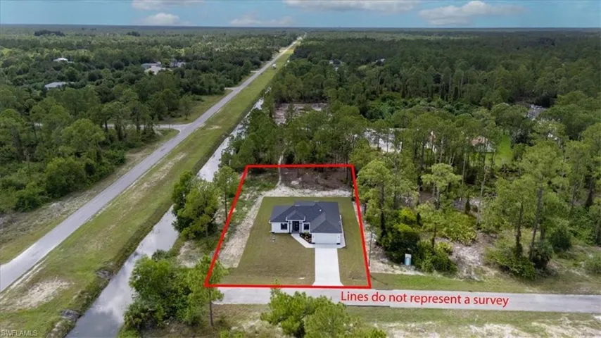 Aerial view of property and surrounding area with property parcel outlined and a heavily wooded area