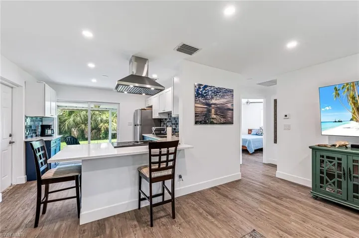 Kitchen featuring island exhaust hood, white cabinetry, backsplash, and light hardwood / wood-style flooring