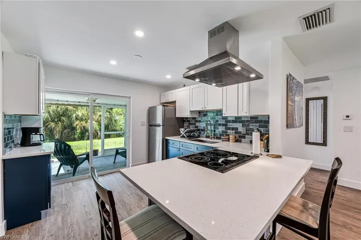 Kitchen featuring island exhaust hood, white cabinets, decorative backsplash, and a breakfast bar area