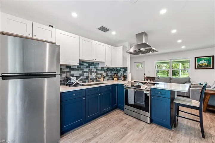 Kitchen with appliances with stainless steel finishes, light hardwood / wood-style flooring, sink, backsplash, and island exhaust hood