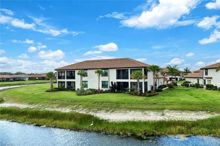 Back of property with a tile roof, a water view, stucco siding, a lawn, and a residential view