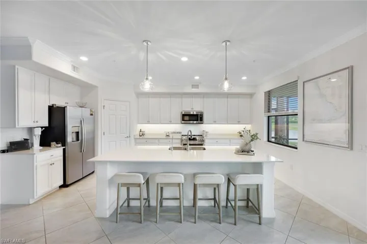 Kitchen featuring appliances with stainless steel finishes, white cabinetry, light tile patterned floors, ornamental molding, and a kitchen breakfast bar