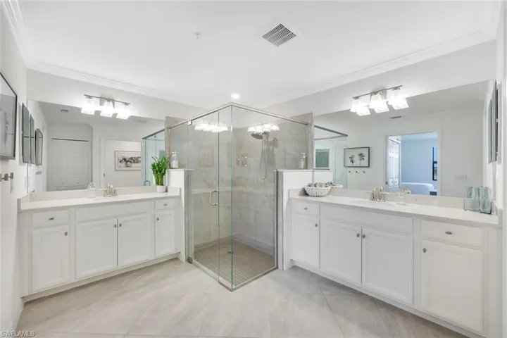 Bathroom featuring crown molding, a shower stall, and two vanities