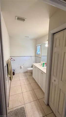 Left Unit: Bathroom with tile walls, wainscoting, double vanity, light tile patterned flooring, and a closet