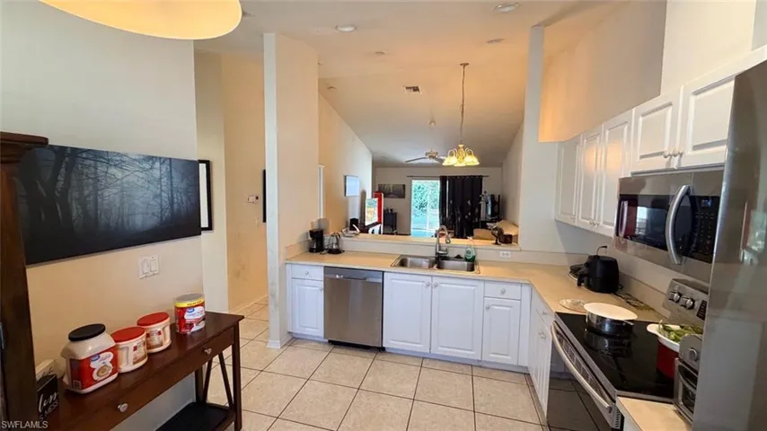 Left Unit: Kitchen with stainless steel appliances, light countertops, lofted ceiling, white cabinetry, and light tile patterned flooring