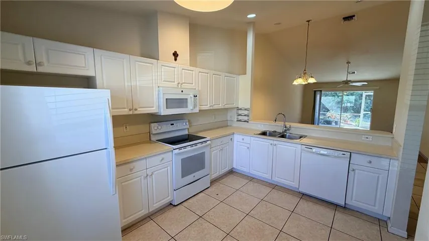 Right Unit: Kitchen featuring white appliances, lofted ceiling, light countertops, white cabinetry, and pendant lighting