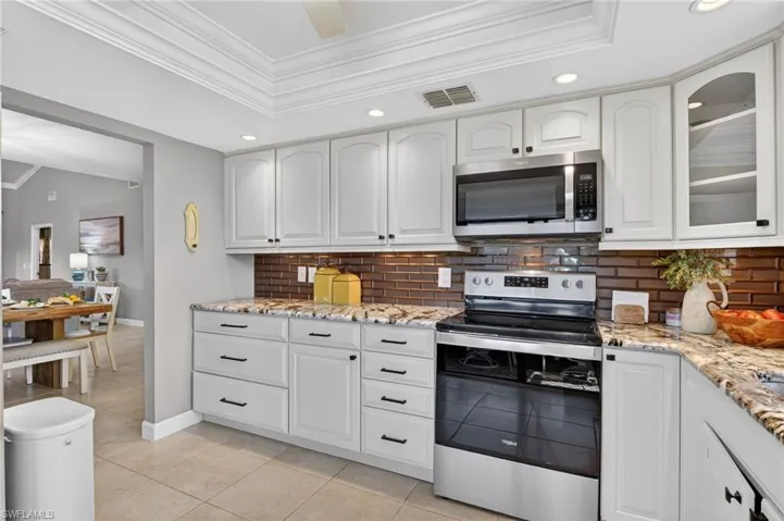 Kitchen featuring ornamental molding, stainless steel appliances, light stone countertops, white cabinetry, and recessed lighting