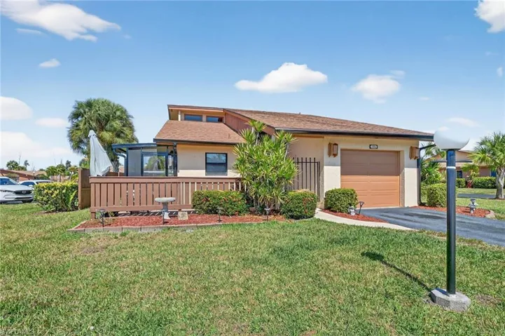 View of front facade featuring a front lawn, stucco siding, roof with shingles, and driveway