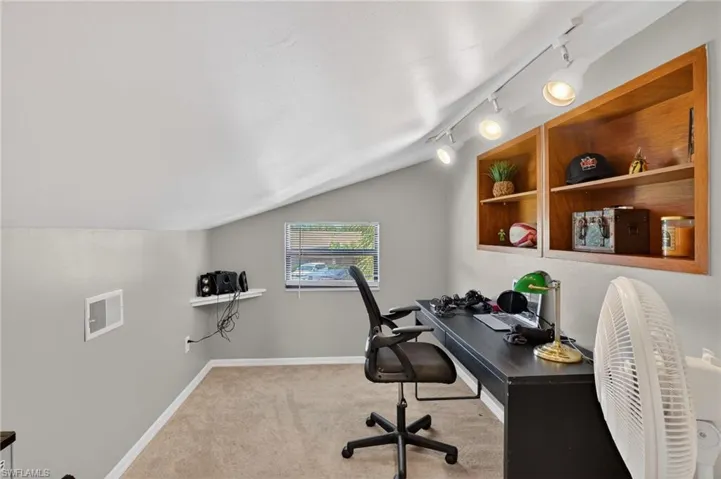 Home office with lofted ceiling, light carpet, and track lighting