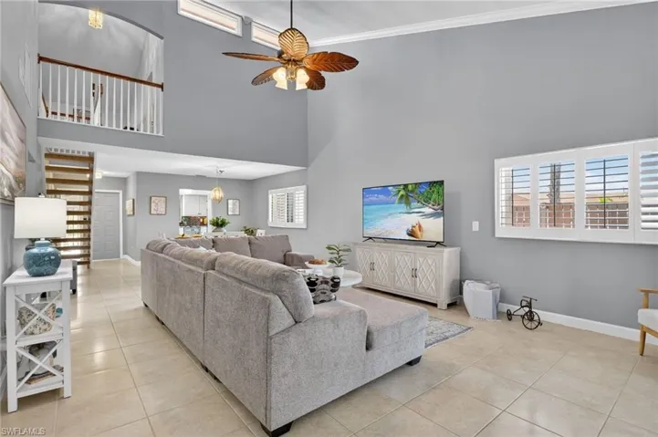 Living room with a ceiling fan, light tile patterned floors, a high ceiling, and ornamental molding