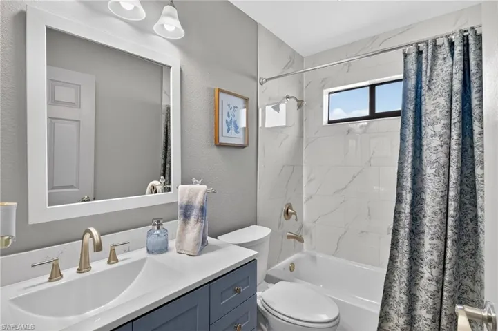 Full bath with shower / bath combination with curtain, vanity, and a textured wall