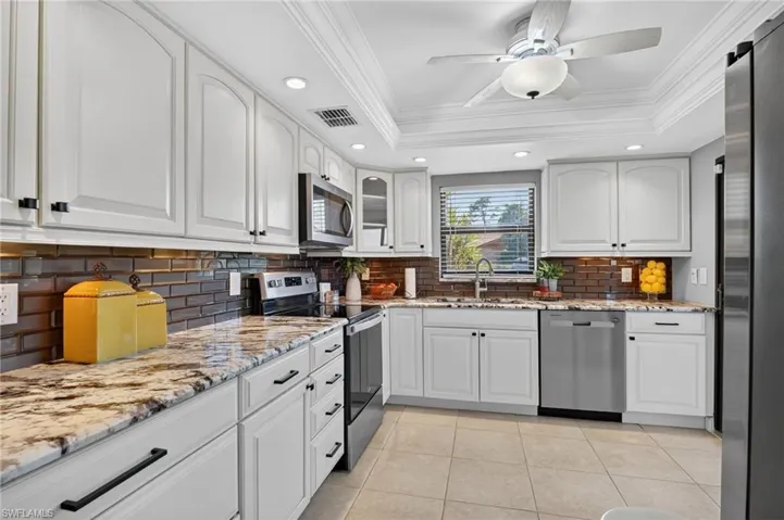 Kitchen with light stone counters, stainless steel appliances, crown molding, recessed lighting, and white cabinets