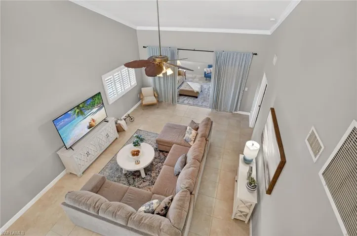 Living room with ceiling fan, a high ceiling, light tile patterned floors, and ornamental molding