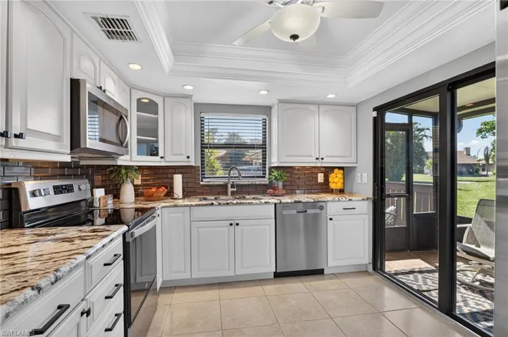 Kitchen with stainless steel appliances, light stone countertops, white cabinetry, glass insert cabinets, and recessed lighting