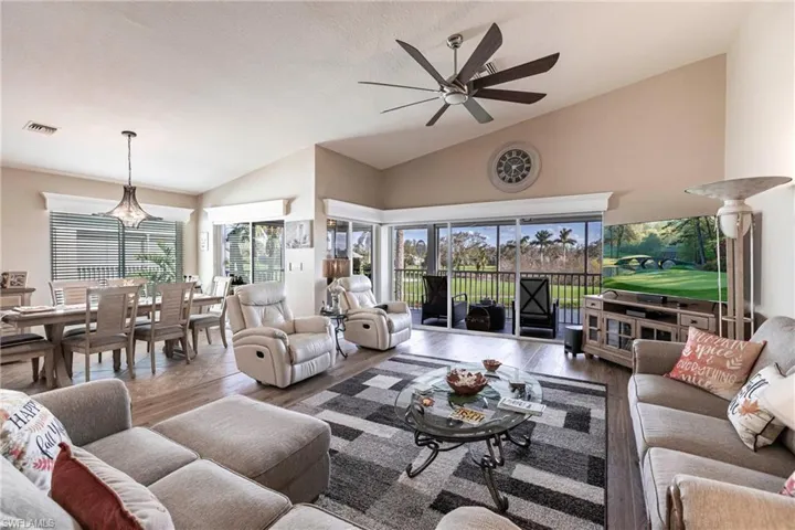 Living room featuring a wealth of natural light, vaulted ceiling, hardwood / wood-style flooring, and ceiling fan with notable chandelier