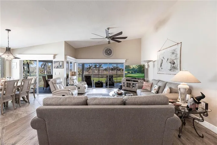 Tiled living room featuring ceiling fan with notable chandelier and vaulted ceiling