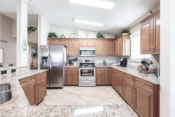 Kitchen with light tile patterned flooring, vaulted ceiling, light stone counters, and appliances with stainless steel finishes