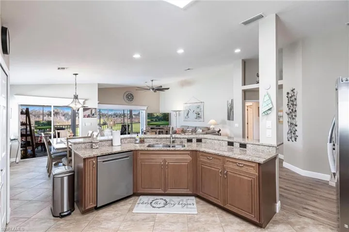 Kitchen featuring stainless steel appliances, sink, decorative light fixtures, and light stone counters