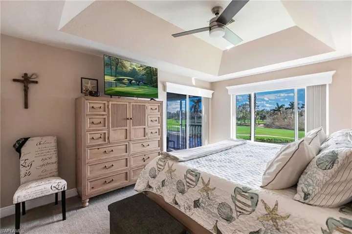Bedroom with a tray ceiling, light colored carpet, ceiling fan, and access to exterior