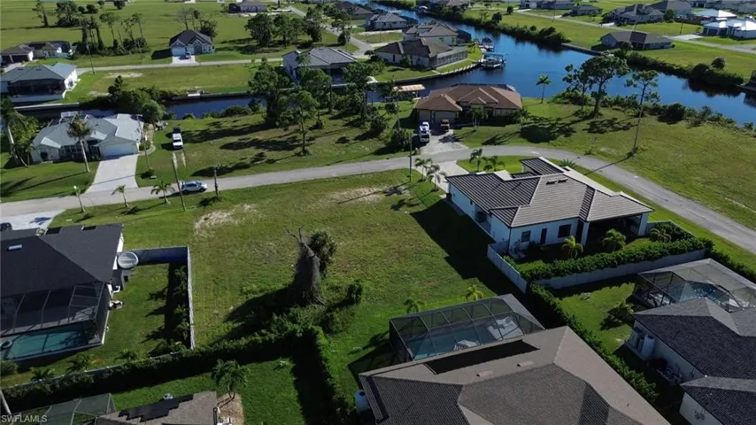Aerial view showcasing expansive manicured grounds with mature landscaping, multiple residences featuring dark-roofed architecture, and serene waterfront access visible in the distance across this spacious residential community setting