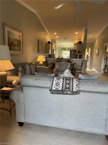 Carpeted living room featuring lofted ceiling, crown molding, and ceiling fan