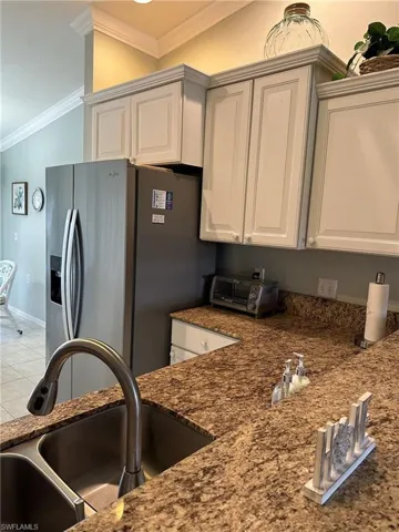Kitchen featuring tile patterned flooring, sink, ornamental molding, white cabinets, and stainless steel fridge with ice dispenser