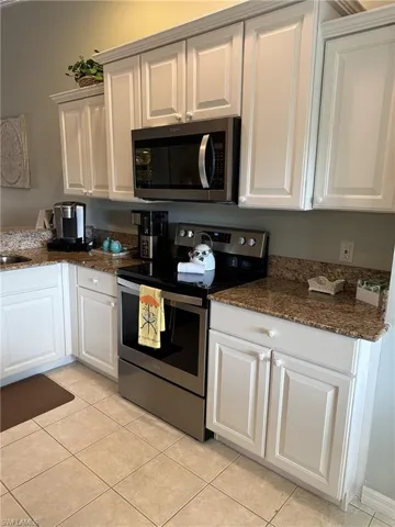 Kitchen with stainless steel appliances, light tile patterned flooring, dark stone countertops, and white cabinets