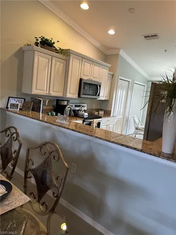 Kitchen featuring white cabinets, ornamental molding, kitchen peninsula, stainless steel appliances, and dark stone countertops